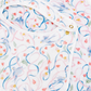 A close-up of a white baby bib with a colorful watercolor-style floral and swirl pattern in blue, pink, and green, featuring white trim and snap closures.