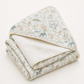 A folded baby blanket with a soft, textured off-white reverse side and a printed front side featuring a safari animal pattern in muted green, blue, and beige tones, set against a plain off-white background.