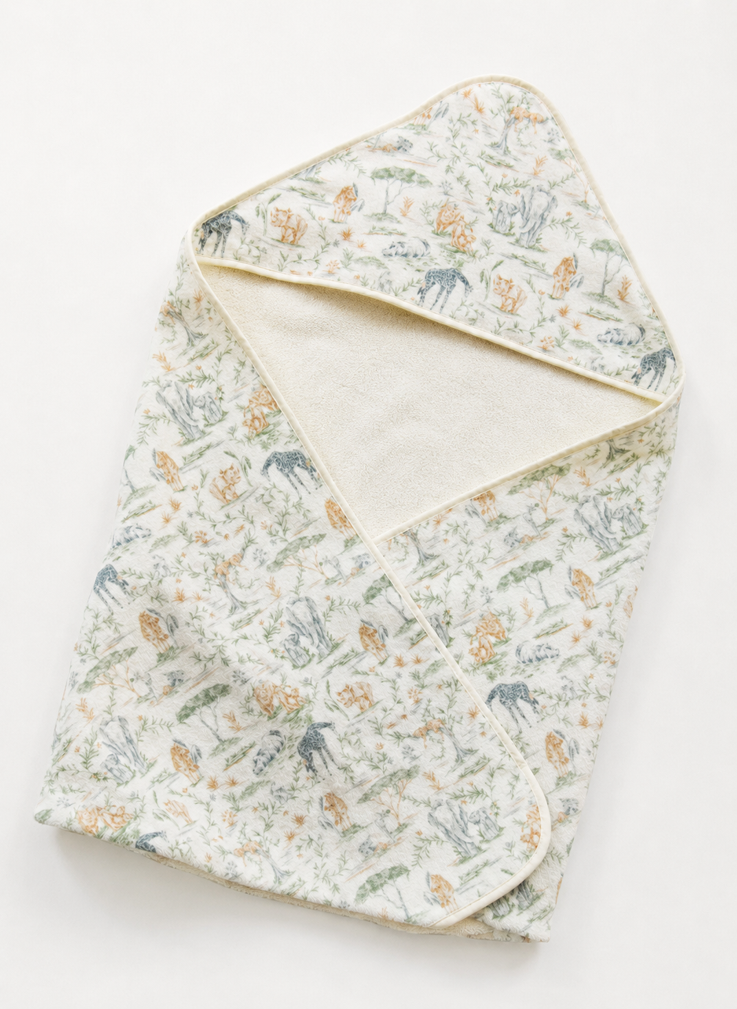 A folded baby blanket or swaddle with a delicate woodland print featuring deer, rabbits, and mushrooms on a cream background, with a solid cream inner lining and trim.