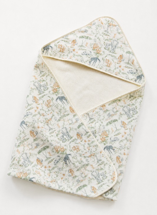 A folded baby blanket or swaddle with a delicate woodland print featuring deer, rabbits, and mushrooms on a cream background, with a solid cream inner lining and trim.