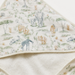 A close-up of a hooded baby towel or wrap with a soft safari animal print on an off-white background. The print features illustrated giraffes, lions, zebras, and trees in muted beige, brown, and gray tones.