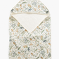 A folded baby wrap blanket with a hood, featuring a delicate woodland animal and plant pattern in muted green, blue, and orange on an off-white background, with a solid cream lining visible inside the hood.