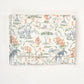 A folded fabric item, likely a blanket or cloth bag, featuring a toile-style safari print with animals and foliage on a cream background.