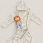 A baby hooded bathrobe with a soft cream background and a light blue and beige animal print, styled with a plush lion toy on the front, set against a neutral light beige background.