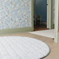 Round rug on a wooden floor with floral wallpaper in the background