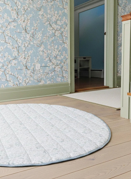 Round rug on a wooden floor with floral wallpaper in the background