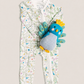 A baby's full-zip footless one-piece romper in white with a colorful bird and floral print, styled with a blue and yellow plush toy chick on a light beige background.