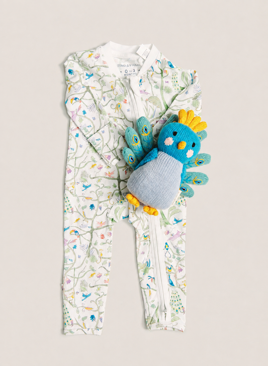 A baby's full-zip footless one-piece romper in white with a colorful bird and floral print, styled with a blue and yellow plush toy chick on a light beige background.