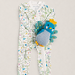 A baby's footed zip-up sleeper with a white background and a colorful bird and floral print, styled with a blue and yellow plush bird toy on a light beige background.