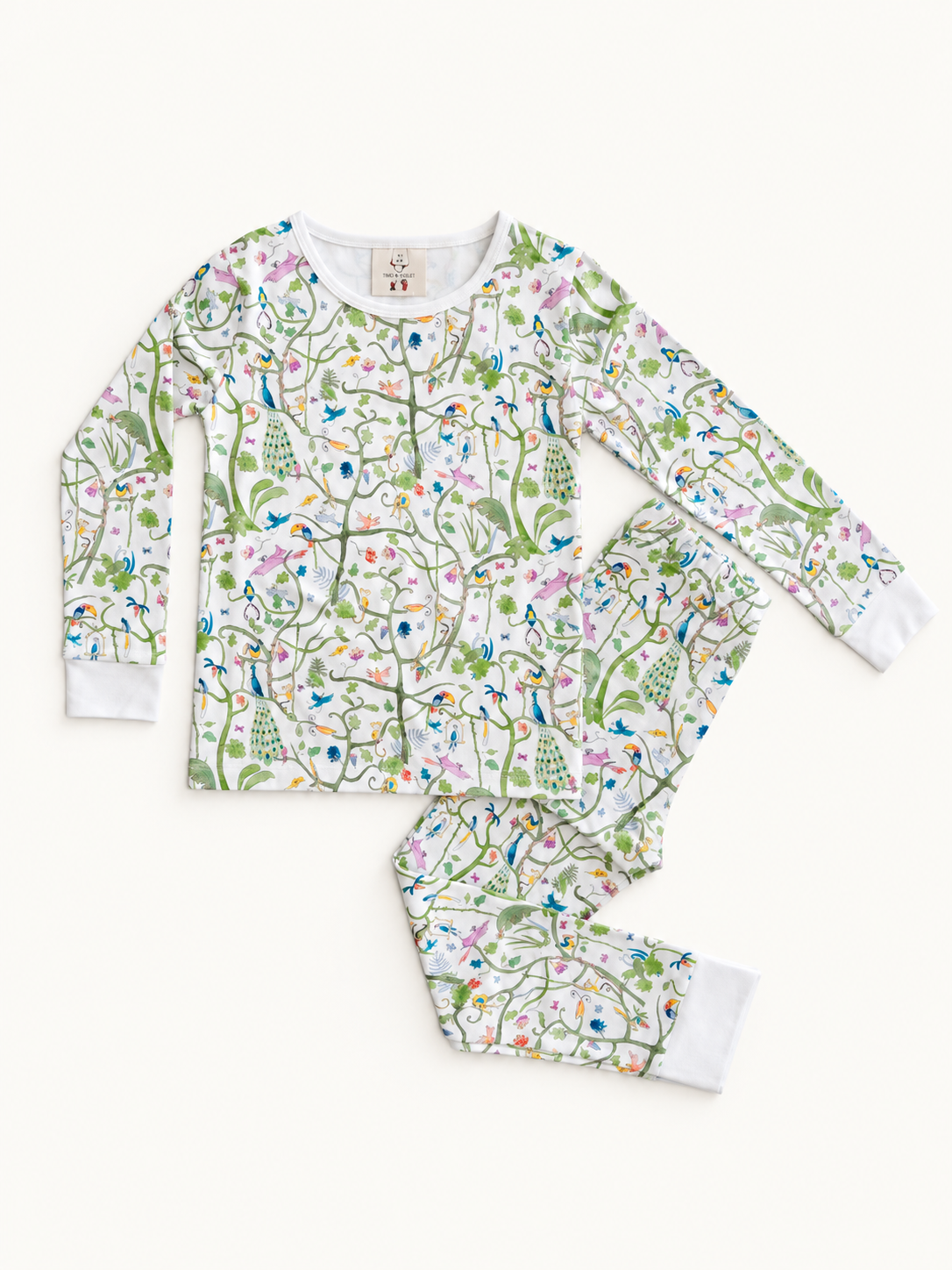 A two-piece long-sleeve pajama set with a white background and a dense, colorful botanical and bird pattern, laid flat on a light cream background.