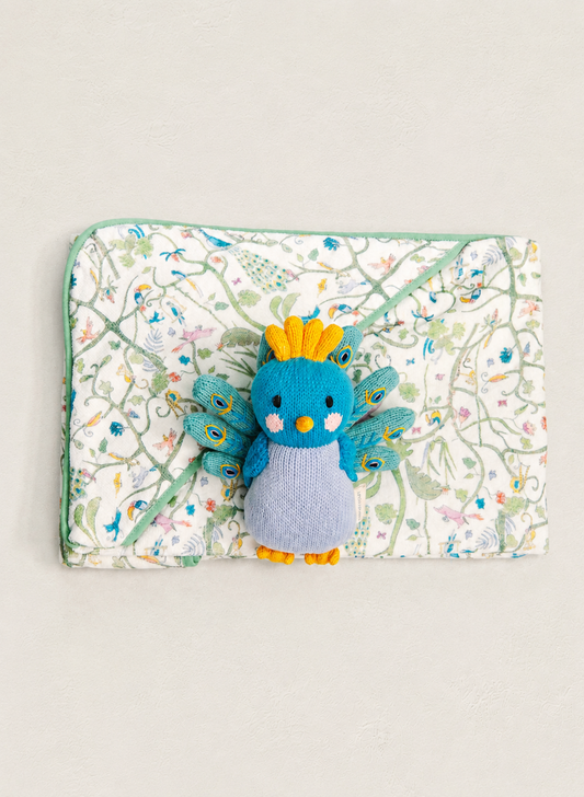 A blue and gray plush bird toy with yellow accents is placed on top of a square quilted fabric pouch featuring a delicate multicolor floral and vine pattern on a white background.