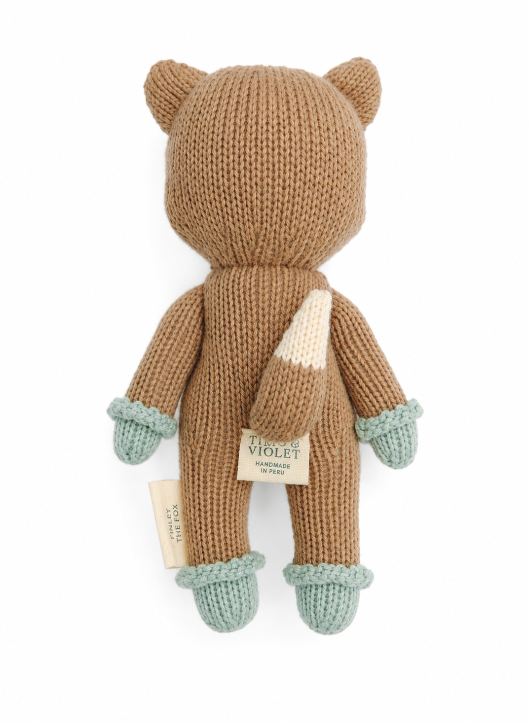 A knitted plush toy shaped like a fox, shown from the back on a plain white background. The body is a warm camel brown, with a cream-colored tail, light blue-green paw cuffs, and matching light blue-green paws.