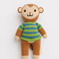 A handmade knitted monkey doll with a brown and beige body, wearing a green and blue striped sweater, photographed against a clean white background.