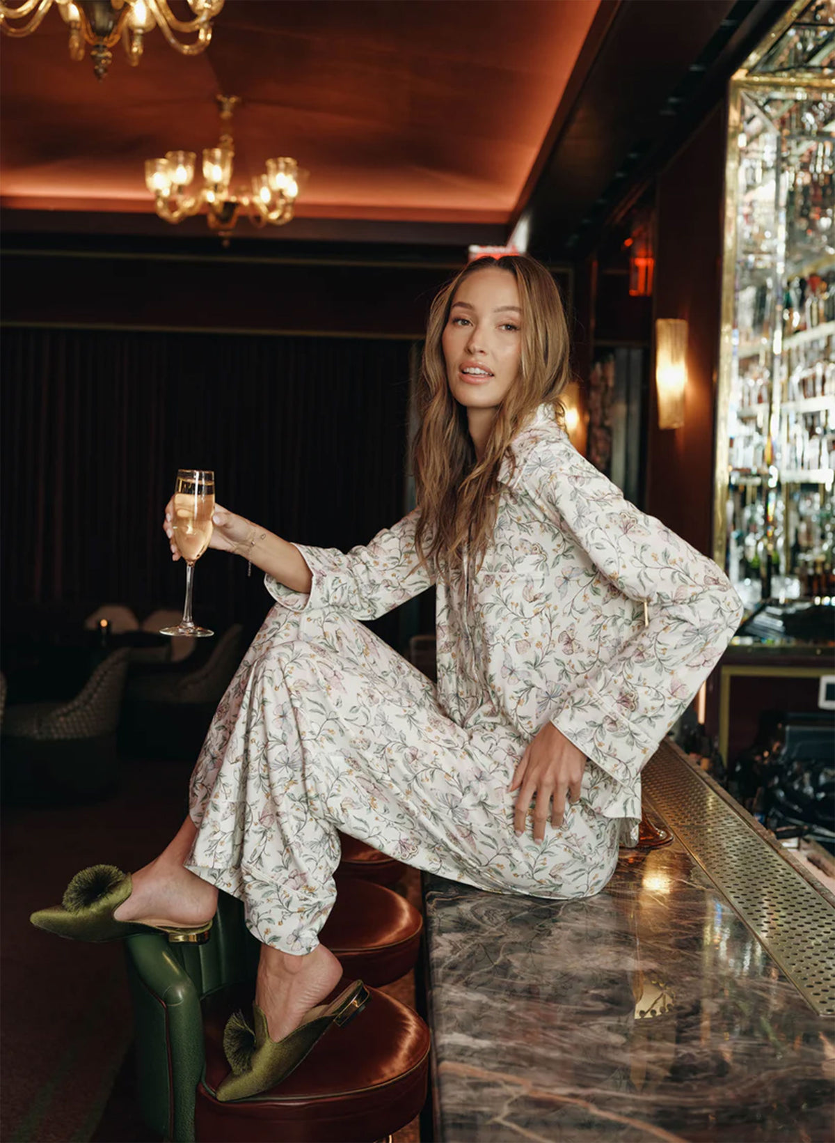 Woman in a floral outfit holding a glass of champagne in a bar setting