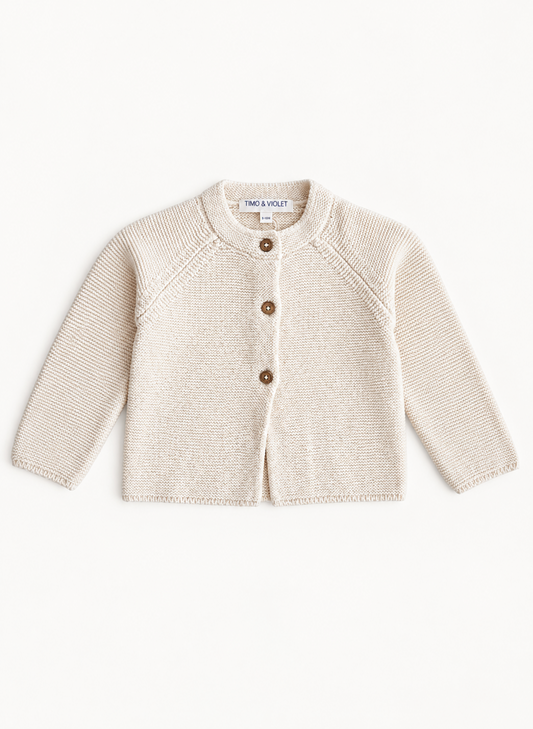 A cream-colored knit cardigan sweater for toddlers, featuring a round neck, raglan sleeves, and three brown buttons down the front. The brand name 'TMC & VLOT' is visible on the inner neck label.