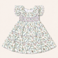 A toddler girl's dress with a white base and a delicate multicolor floral print, featuring ruffled cap sleeves and a smocked waist, shown flat on a light beige background.