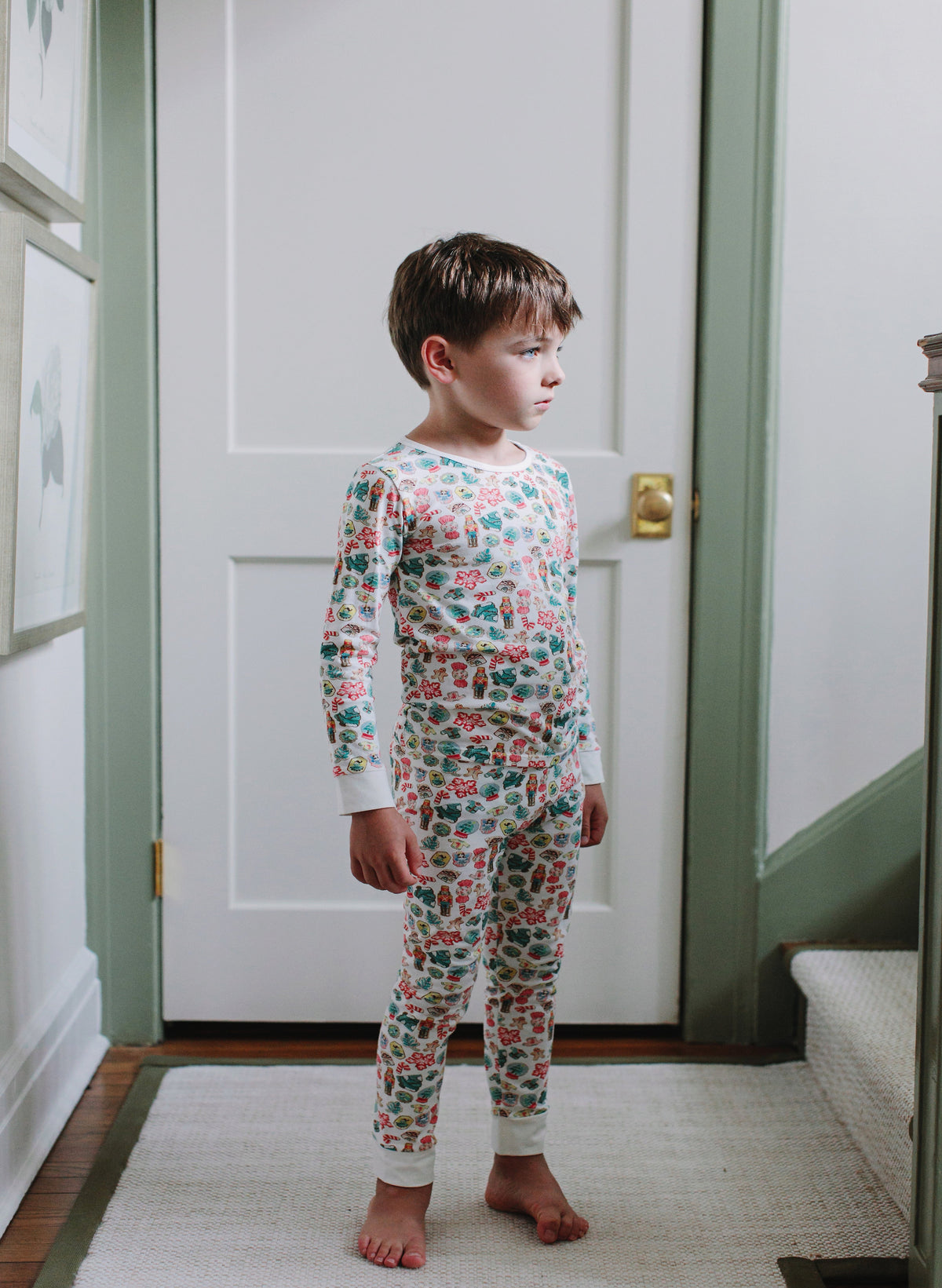 Child wearing a floral pajama set standing in a room with a white door and green trim.